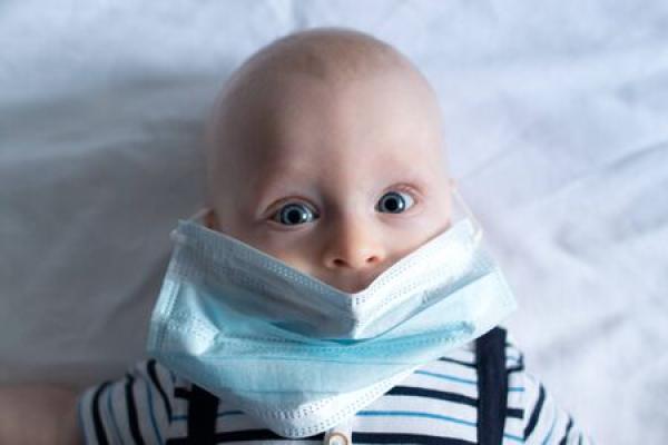 A baby lays on a white cloth with a blue face mask on